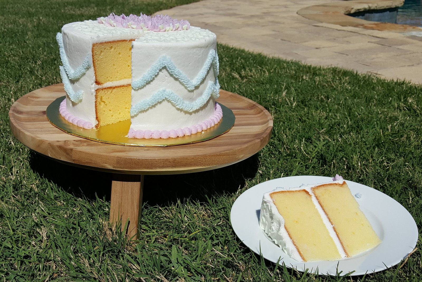 A frosted yellow layer cake on a stand with a full slice served alongside